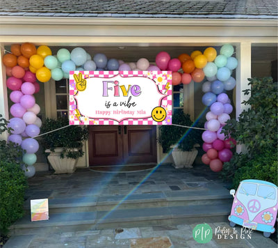 five is a vibe birthday banner with pink checkers, smiley face, retro peace signs, daises and lightening bolts in front of house with rainbow balloon garland