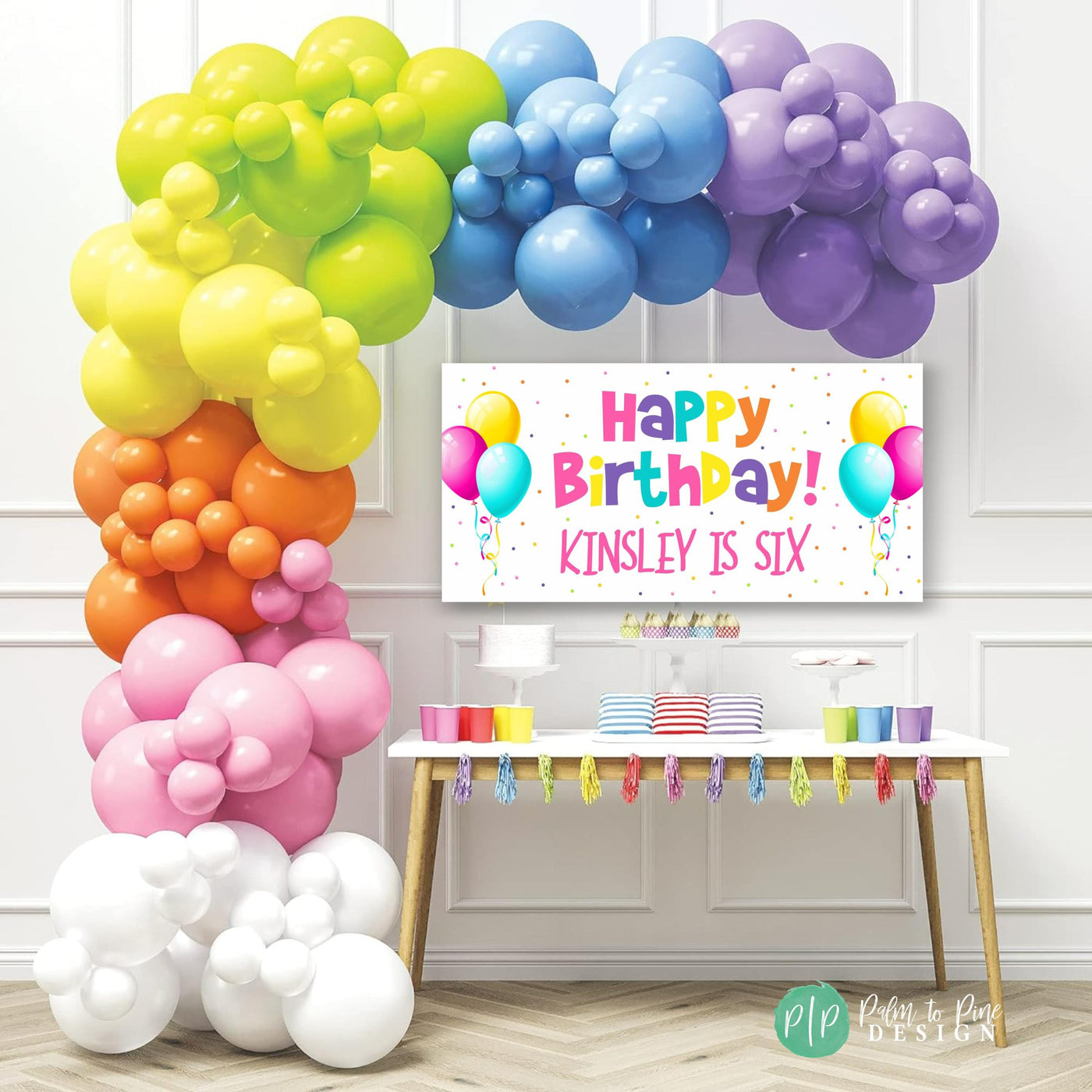 girls happy birthday banner with balloons in rainbow colors with polka dots in front of a dessert table with a balloon garland